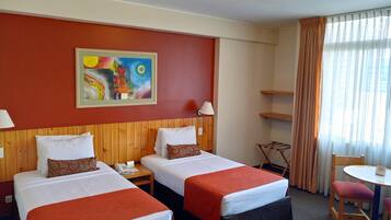 A hotel room with two beds, a painting on the wall, a desk with a lamp, and a chair.