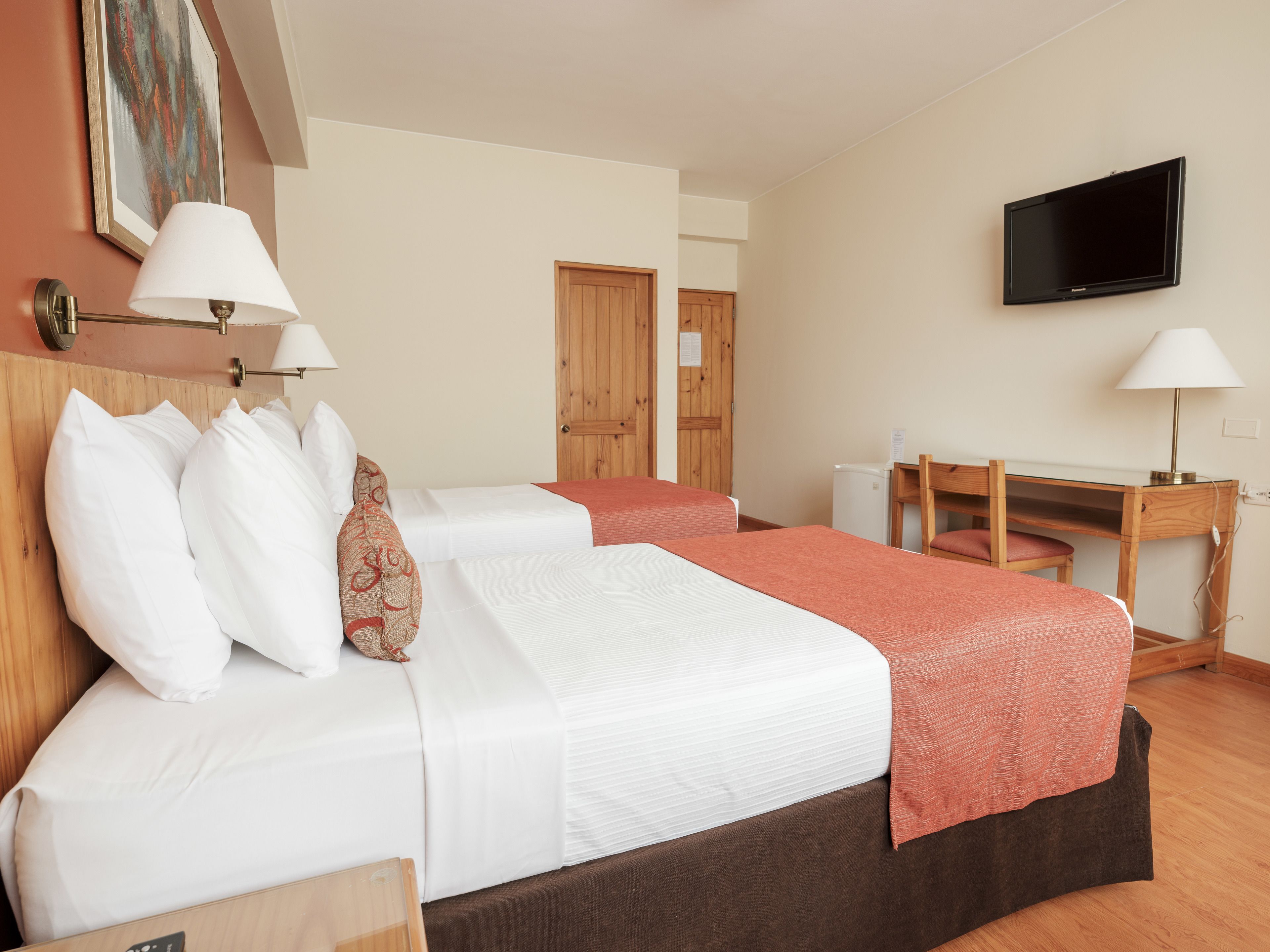 Una habitación de hotel con dos camas, un escritorio, un televisor y una puerta.
