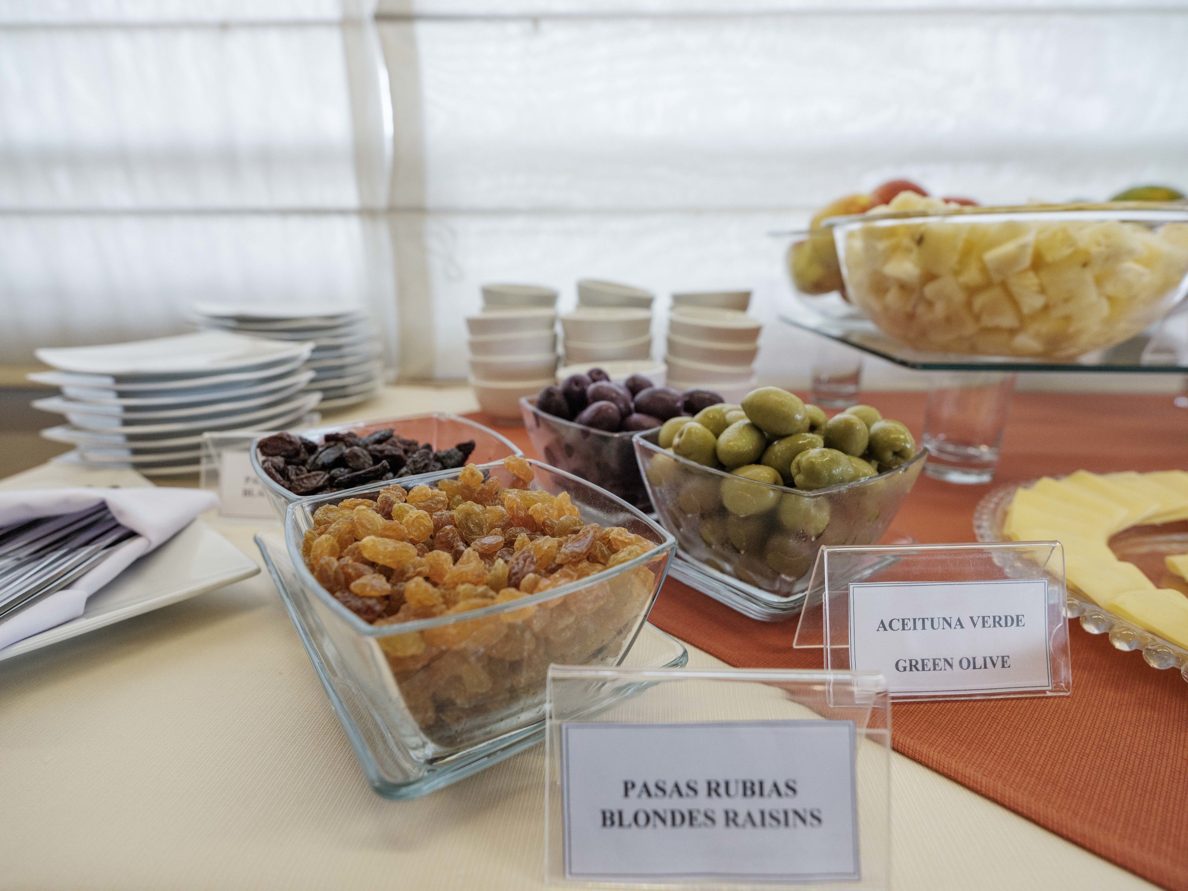 A buffet table with various food items including green olives, raisins, and other snacks.