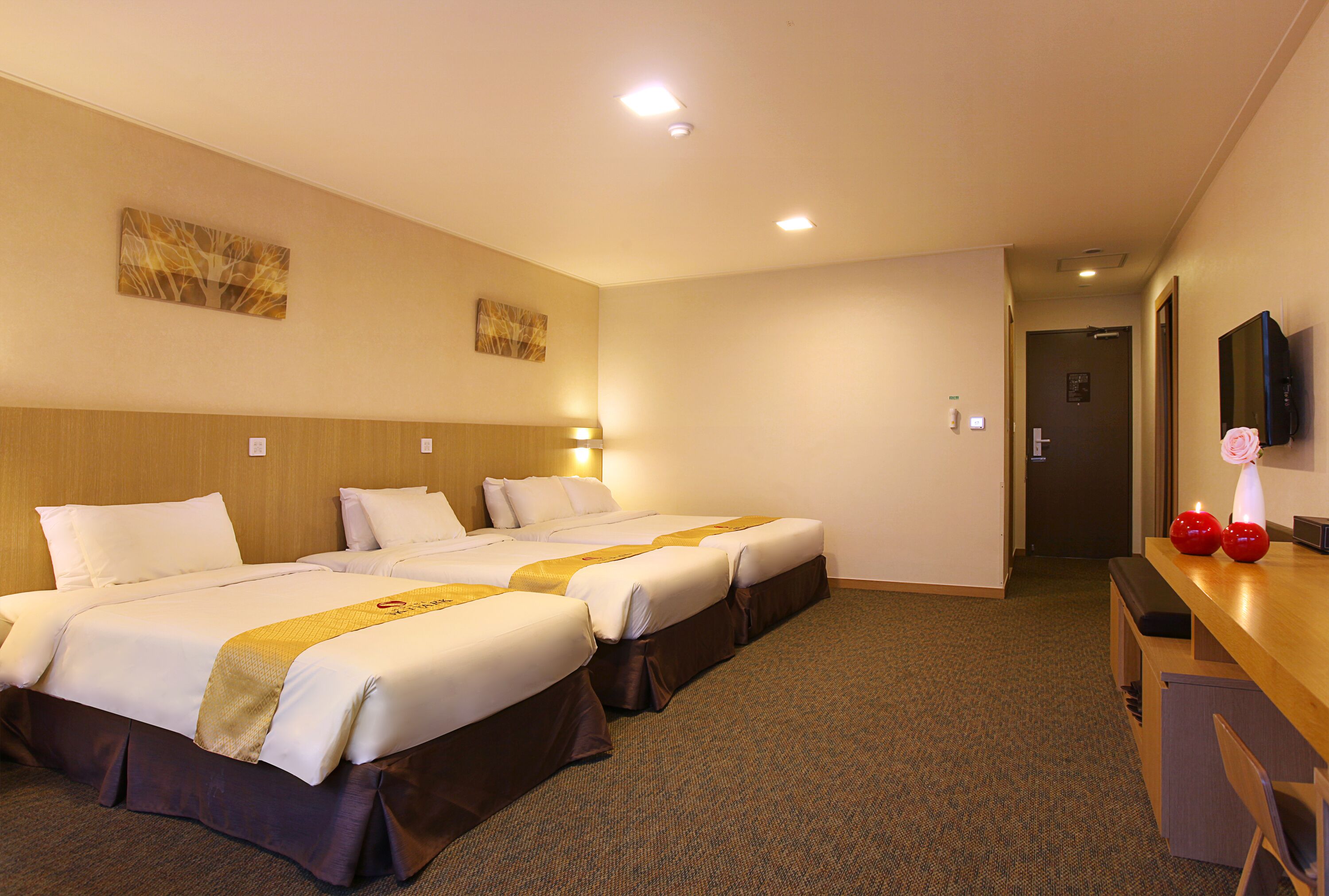 A hotel room with two beds, a wooden headboard, a flat-screen TV, and a desk with a vase.