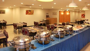 A buffet setup with multiple serving stations, tables, and chairs arranged in a spacious dining area. - Hotel Skypark Jeju 1 (Jeju City)