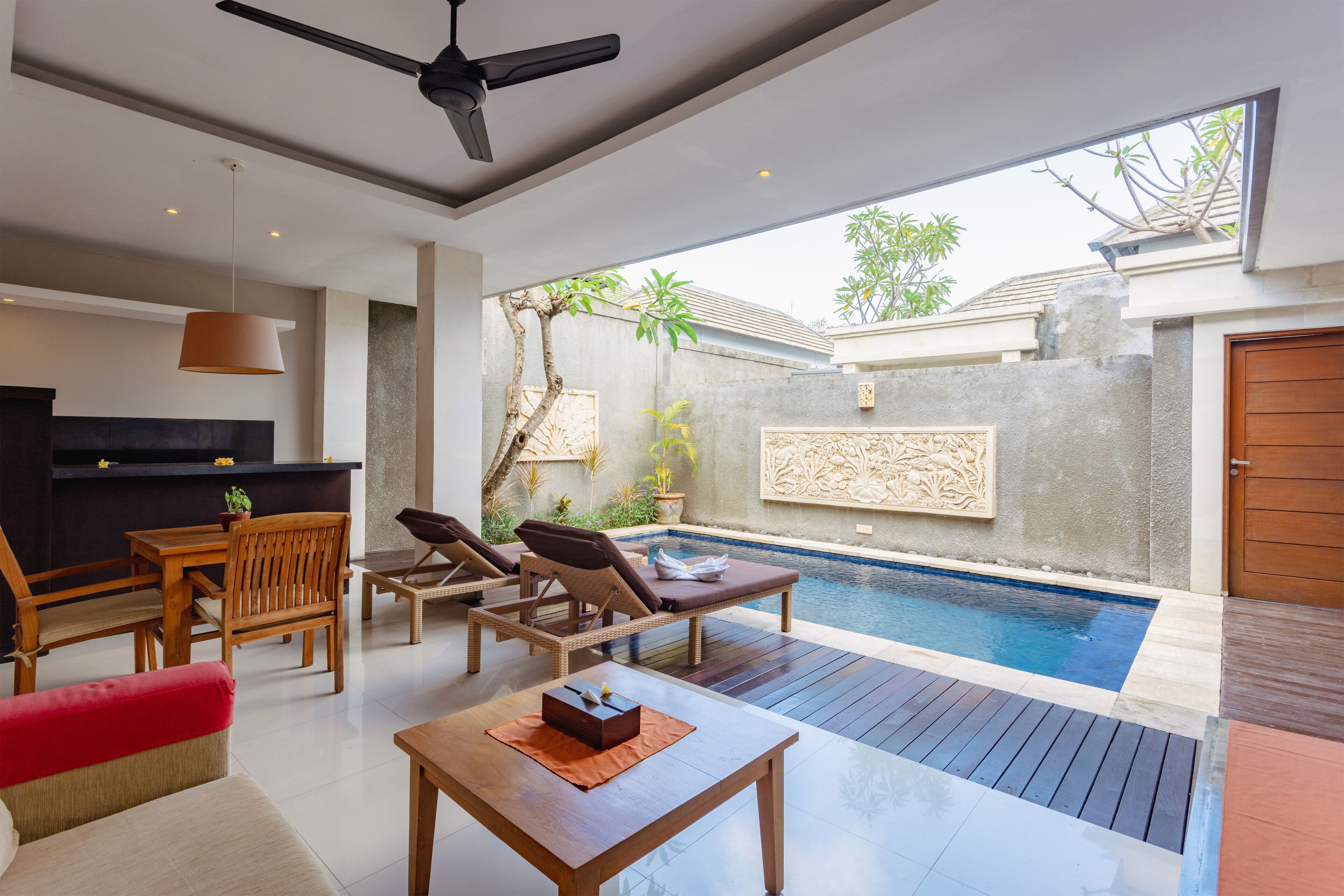 A modern outdoor living area with a pool, wooden furniture, and a ceiling fan.