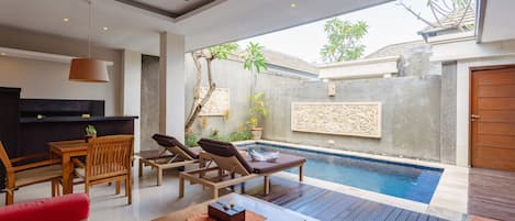 A modern outdoor living area with a pool, wooden furniture, and a ceiling fan.