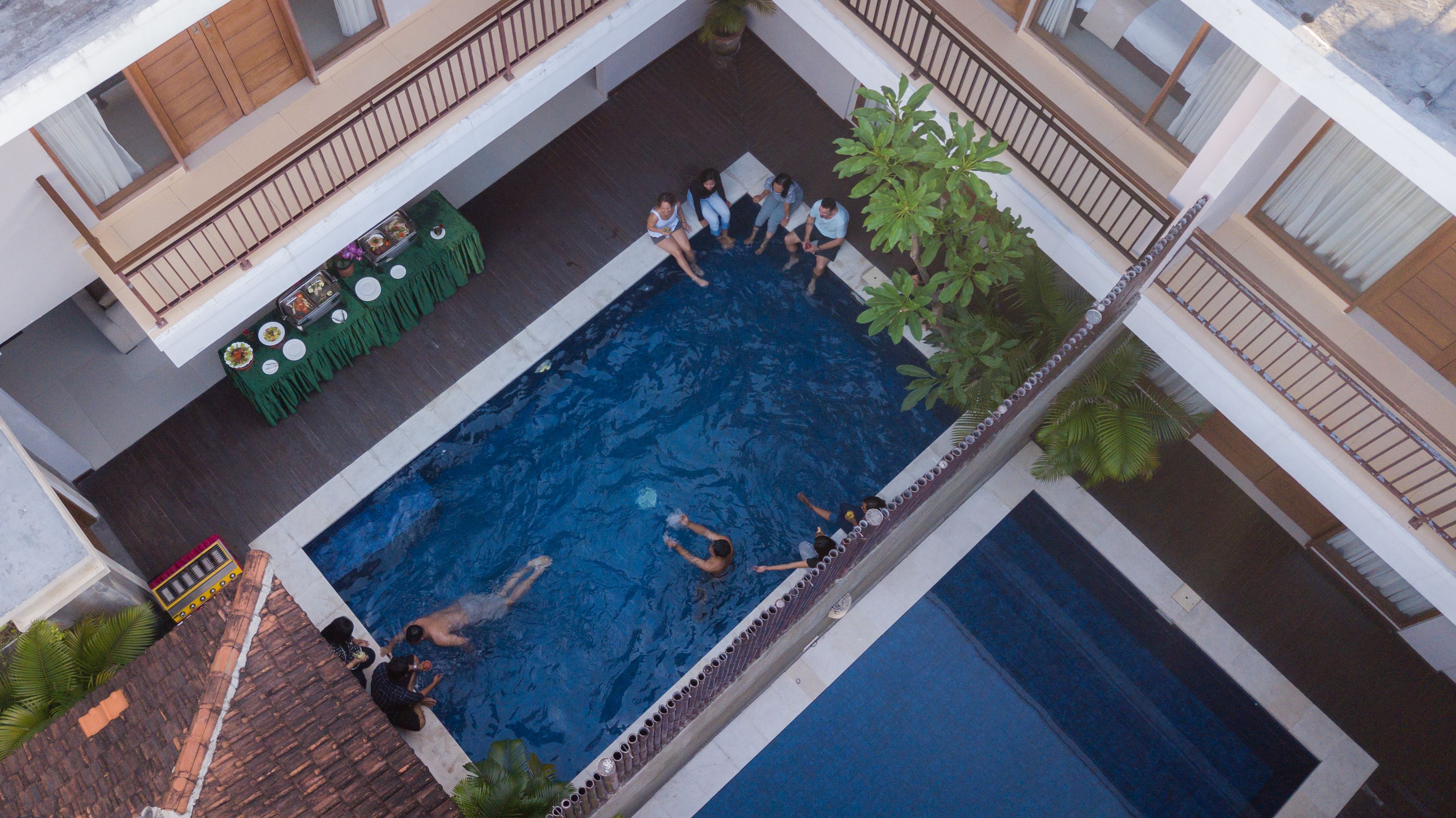 An aerial view of a swimming pool area with a dining setup and surrounding greenery.