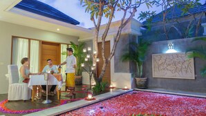 A dining area with a table and chairs, a small garden with a water feature, and a wall with a decorative panel. - The Light Exclusive Villas & SPA (Seminyak)