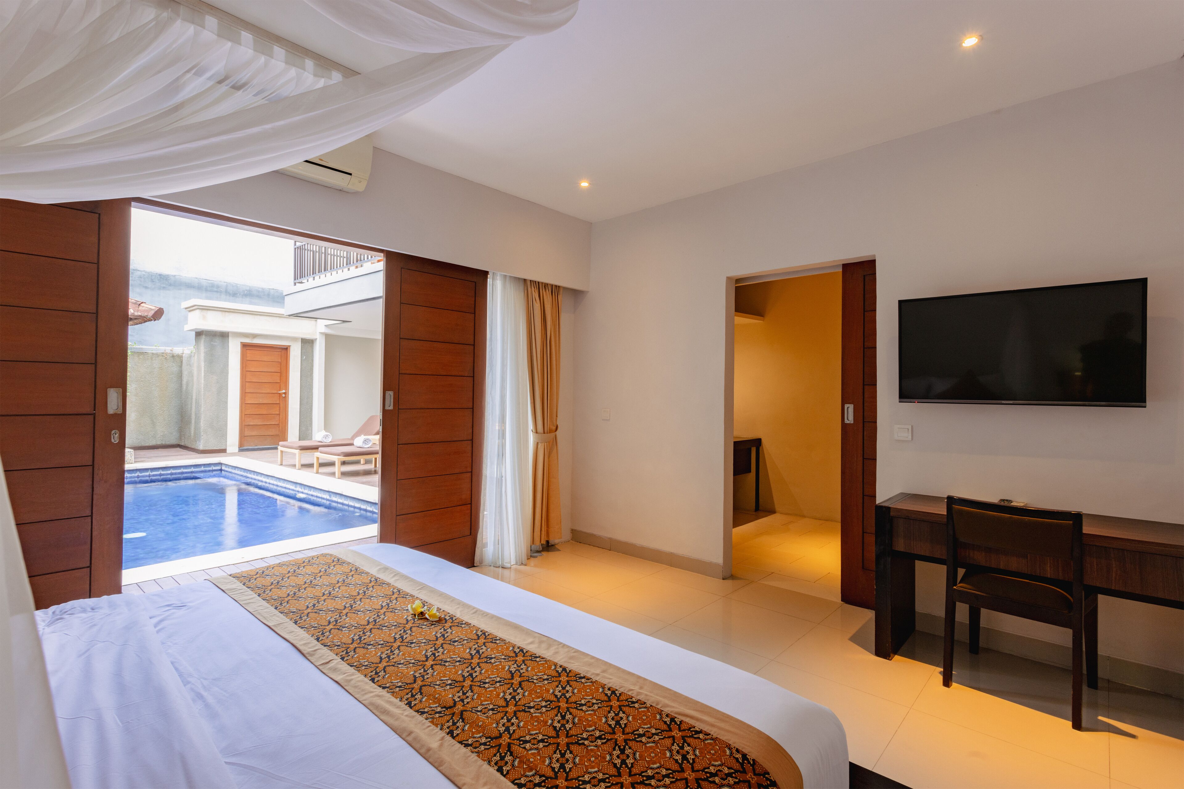 A hotel room with a bed, a desk, a TV, and a view of a pool.