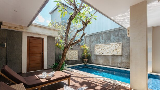 A poolside area with lounge chairs, a wooden door, and a small tree. - The Light Exclusive Villas & SPA (Seminyak)