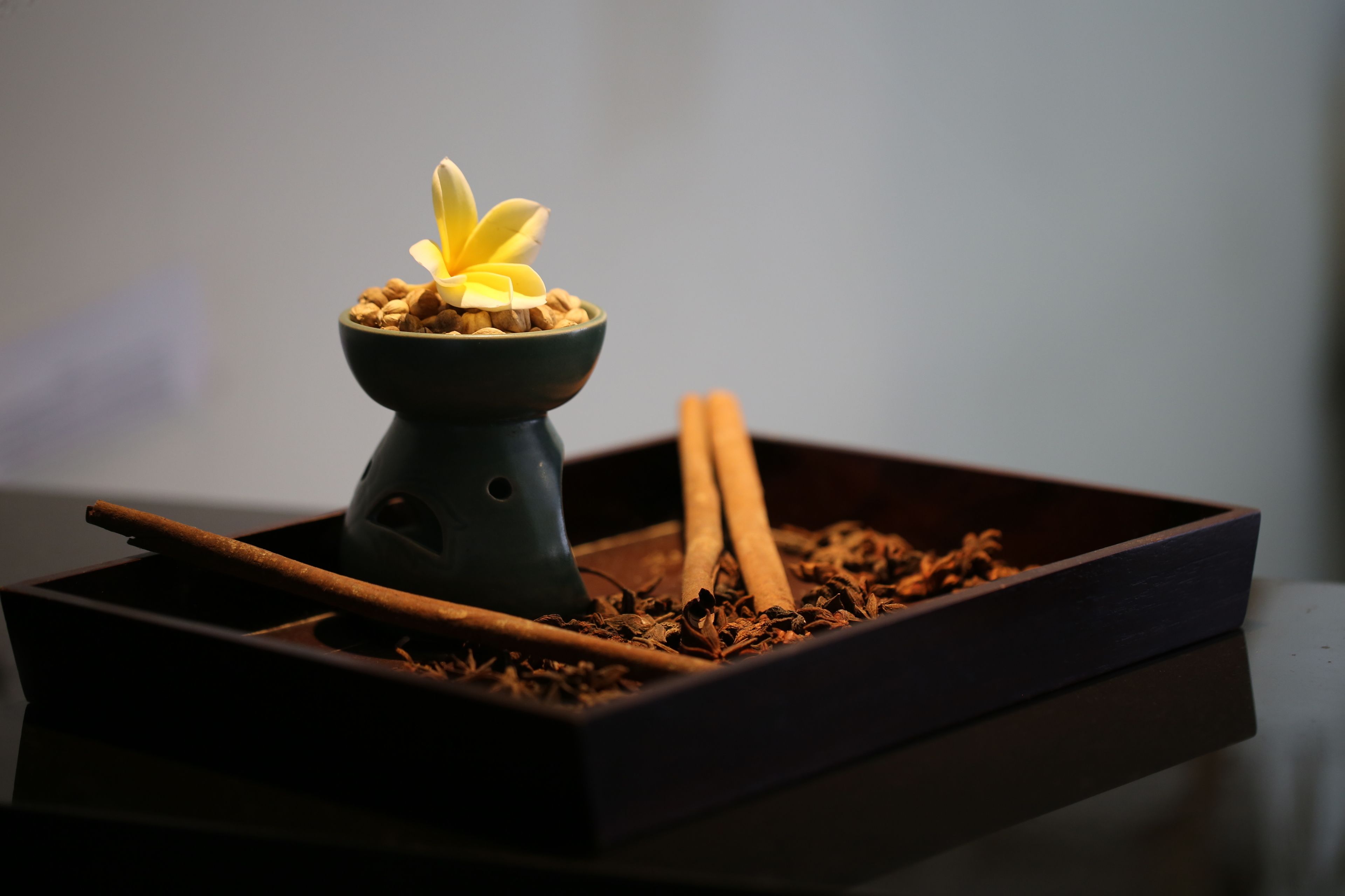 A dark wooden tray with a small bowl containing a yellow flower, cinnamon sticks, and star anise.