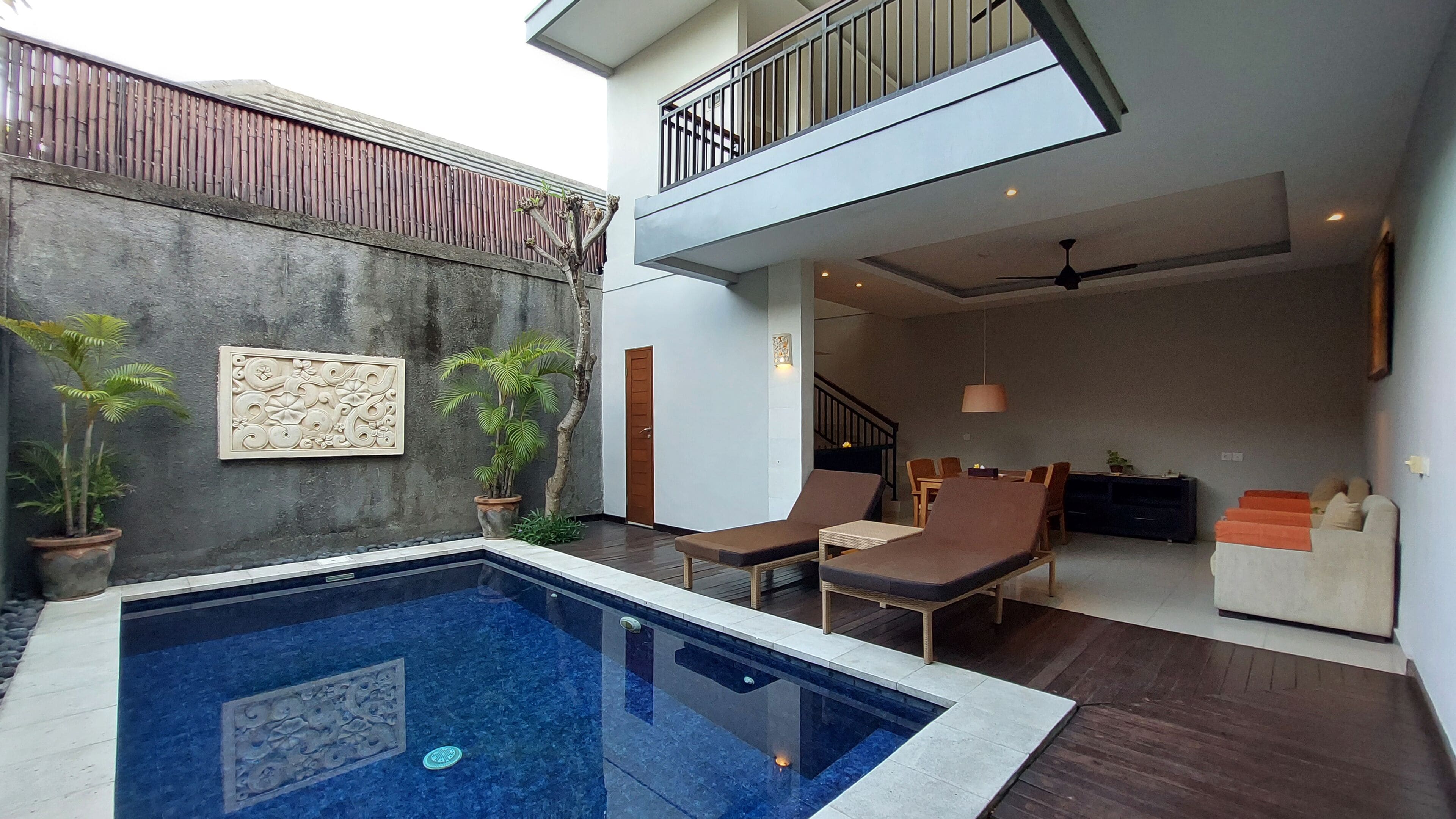 A modern indoor pool area with a clear view of the pool, lounge chairs, and a staircase leading to an upper level.