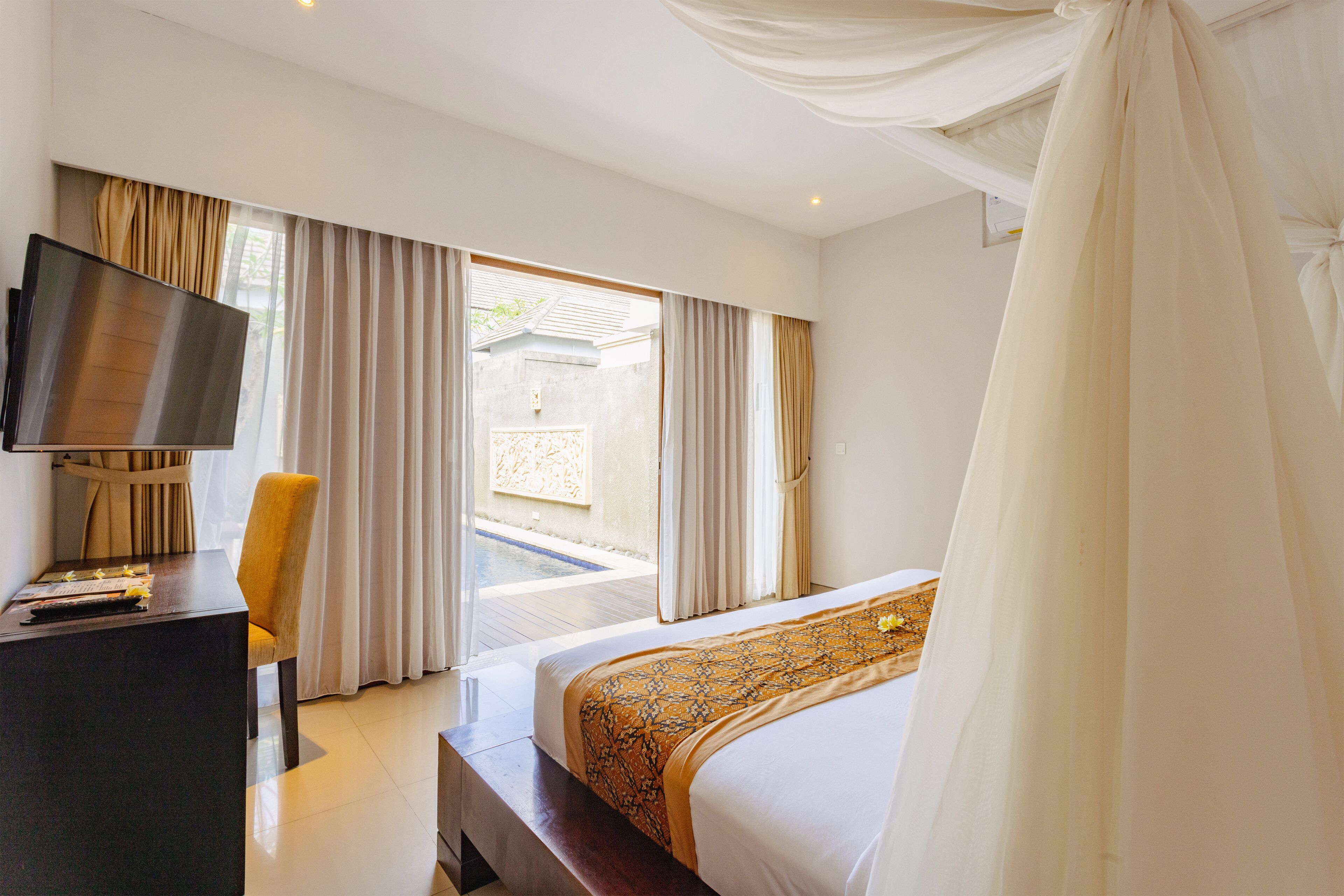 A hotel room with a bed, a desk, a TV, and a view of a pool and outdoor area.