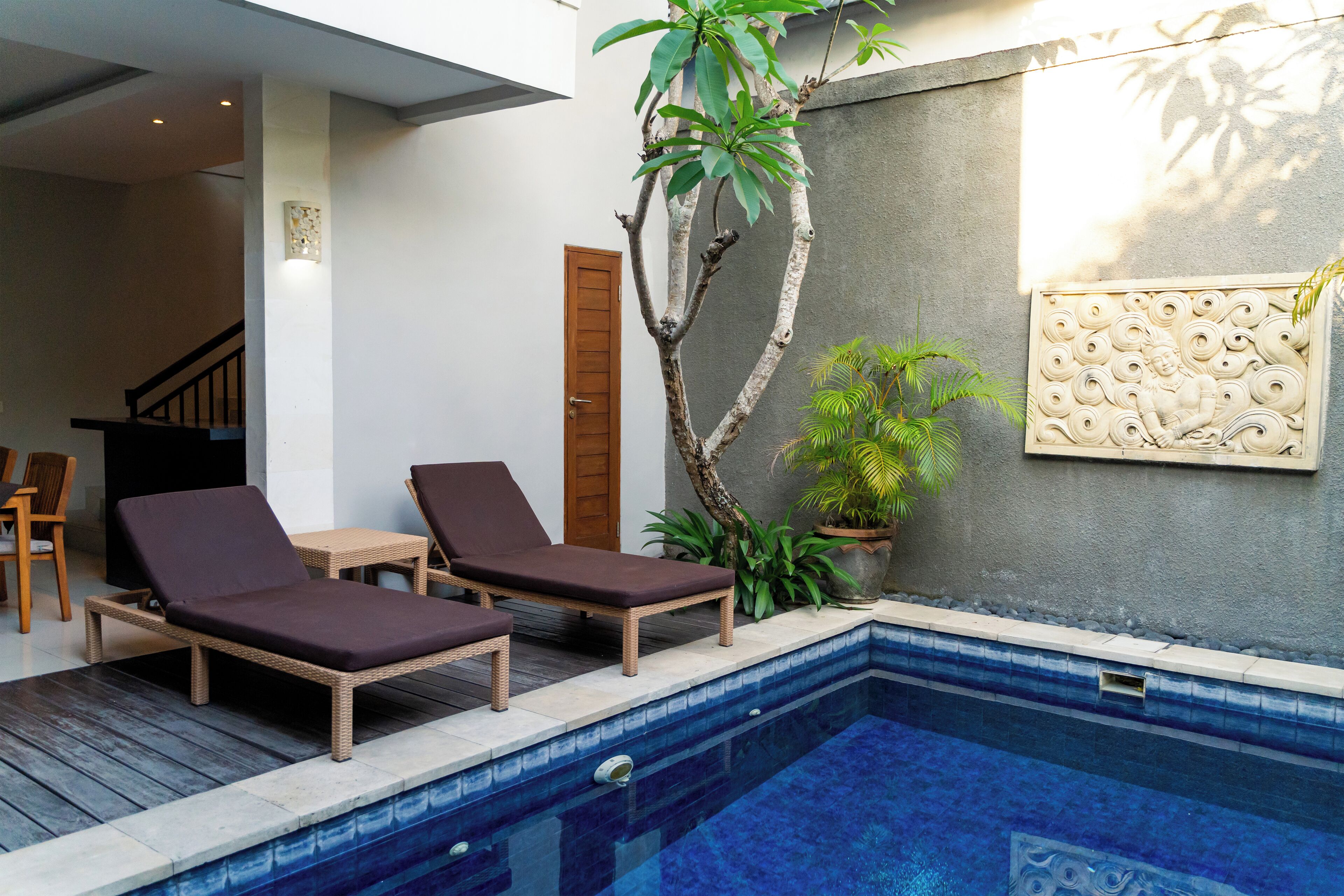 A pool area with two lounge chairs, a wooden table, and a potted plant.