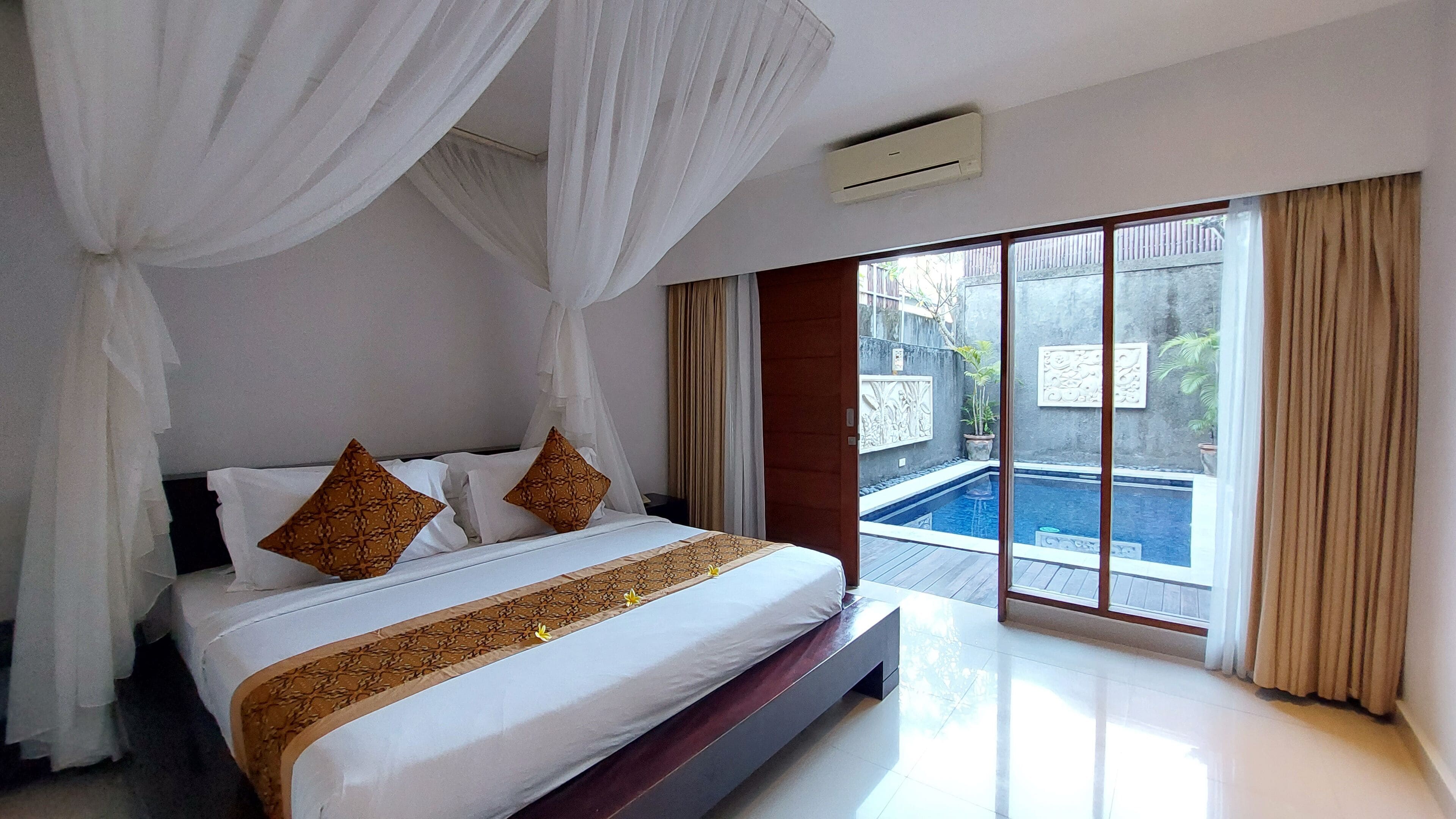 A bedroom with a large bed, white curtains, and a view of a swimming pool.