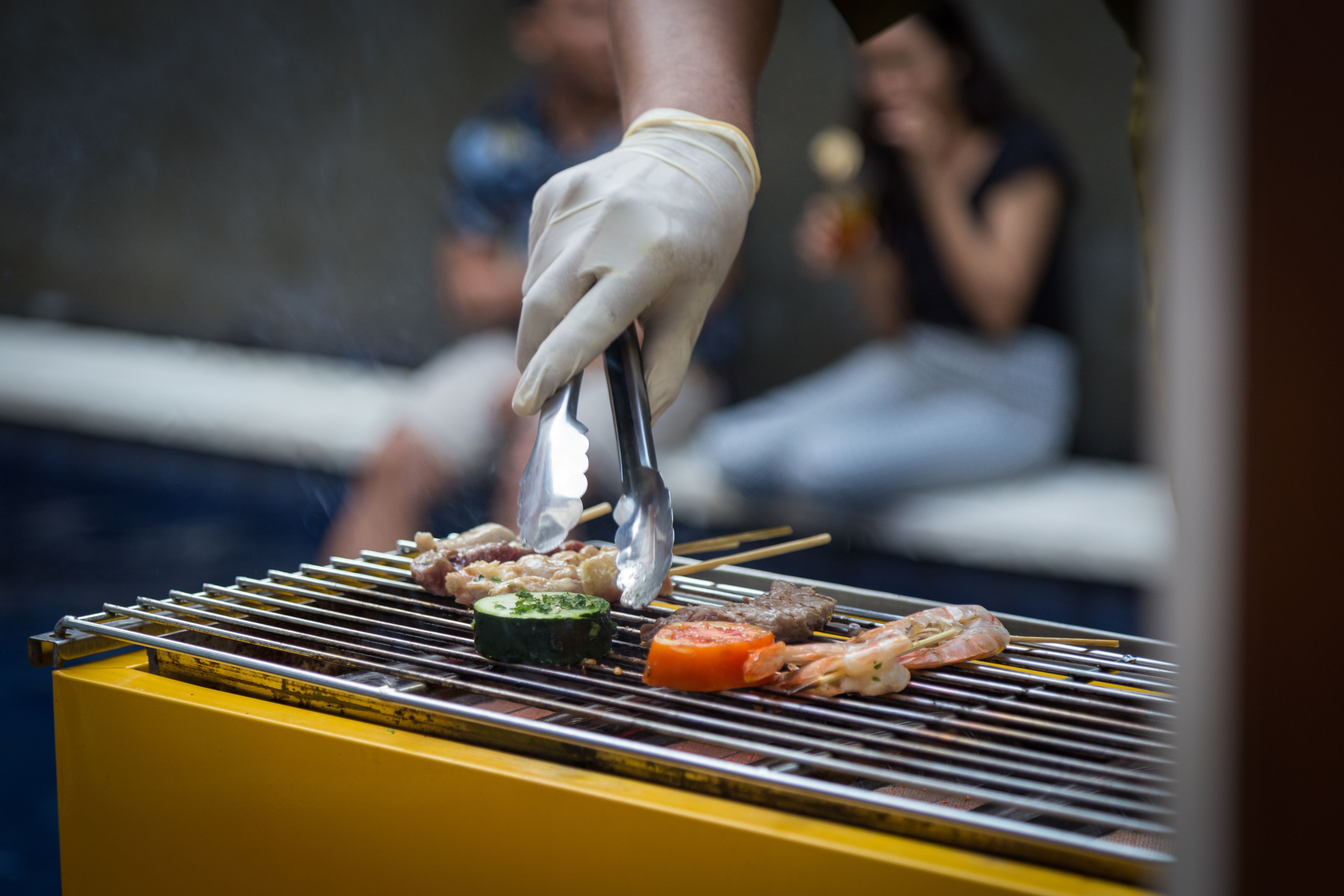 A person grilling vegetables and meat on a portable grill.
