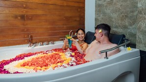 A bathtub filled with colorful flower petals and a person holding a drink. - The Light Exclusive Villas & SPA (Seminyak)