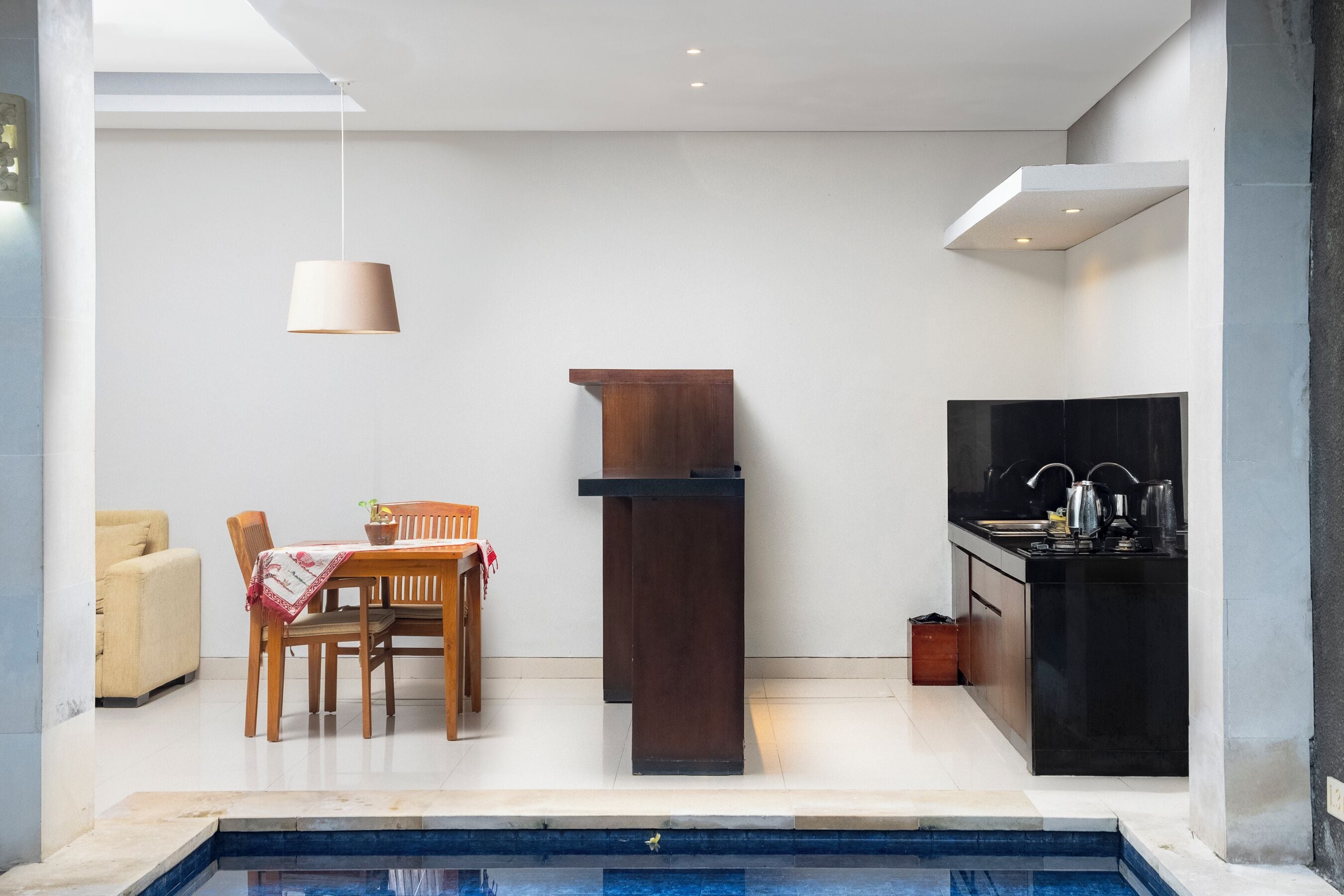 A modern kitchen with a built-in stove, a dining area with a wooden table and chairs, and a small pool area.