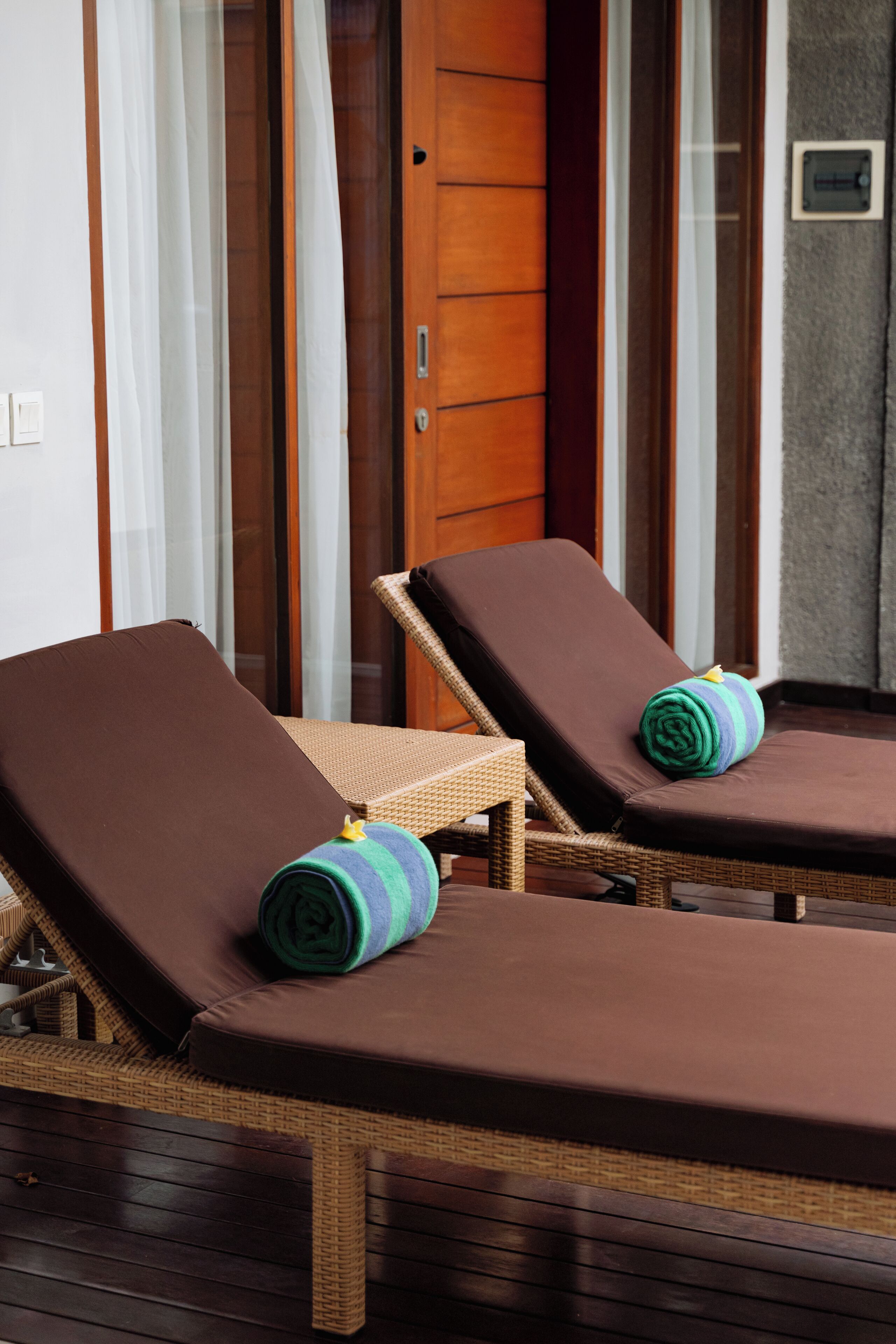 Two wicker lounge chairs with brown cushions and a rolled towel on one.