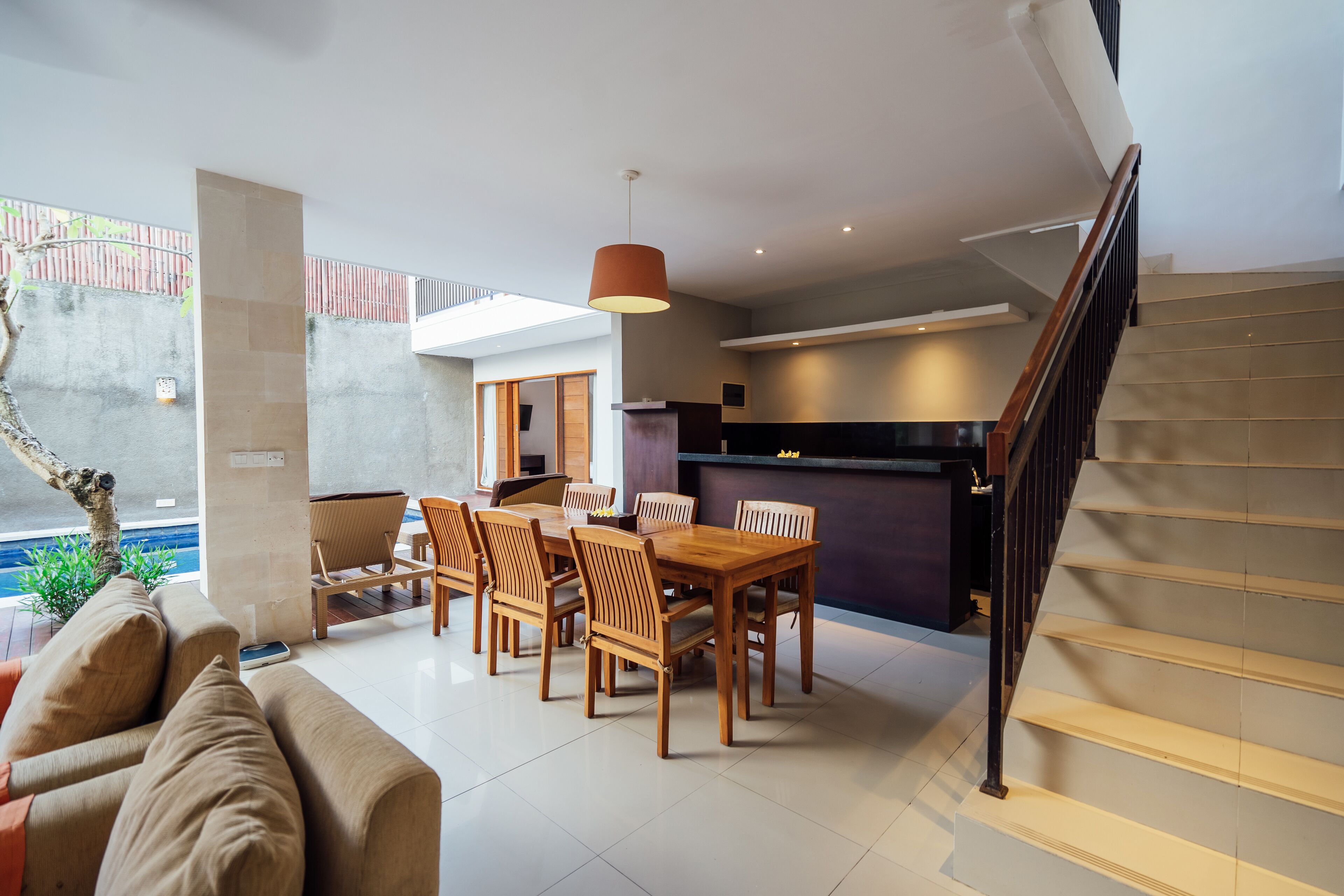 A modern living room with a dining area, a staircase, and a view of a swimming pool.
