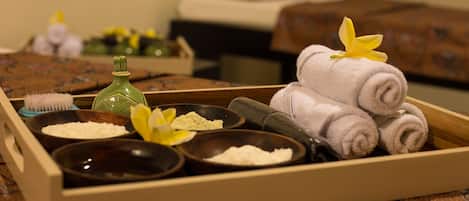 A wooden tray with towels, a bottle, and bowls of bath salts and oils.