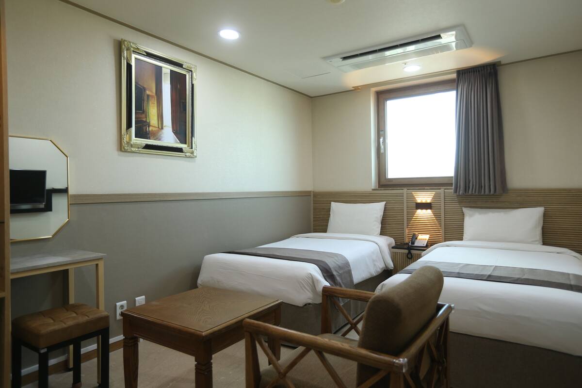 A hotel room with two beds, a desk, a chair, a TV, and a window with curtains.