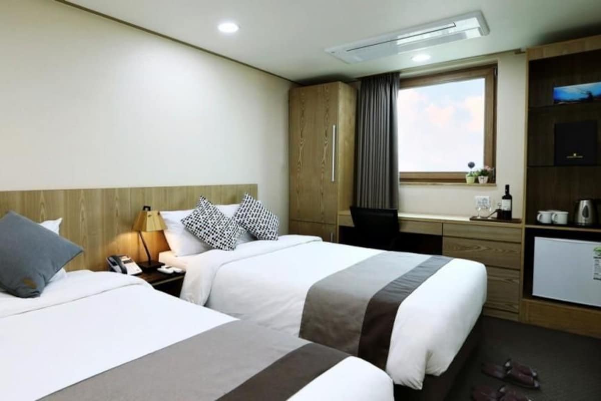 A hotel room with two beds, a desk, a TV, and a window with curtains.