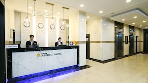 Un mostrador de recepción de hotel con relojes, un cartel con la palabra Seúl y un ascensor.