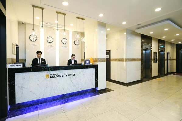 A hotel reception desk with clocks, a sign for Seoul, and an elevator.