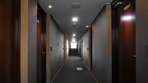 Un largo y estrecho pasillo de hotel con puertas a ambos lados, suelo alfombrado e iluminación empotrada en el techo.