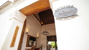 Entrada de un hotel con un arco de madera, un letrero que dice "BIOMA HOTEL BOUTIQUE" y un letrero de "BIENVENIDA".