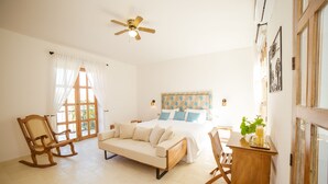 Un dormitorio con una cama, un sofá, un sillón mecedora y una pequeña mesa con una planta.