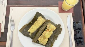 A plate of tamales on a table with a fork, a glass of orange juice, and sunglasses.