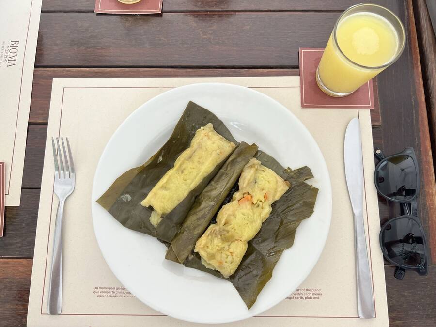 A plate of tamales on a table with a fork, a glass of orange juice, and sunglasses.