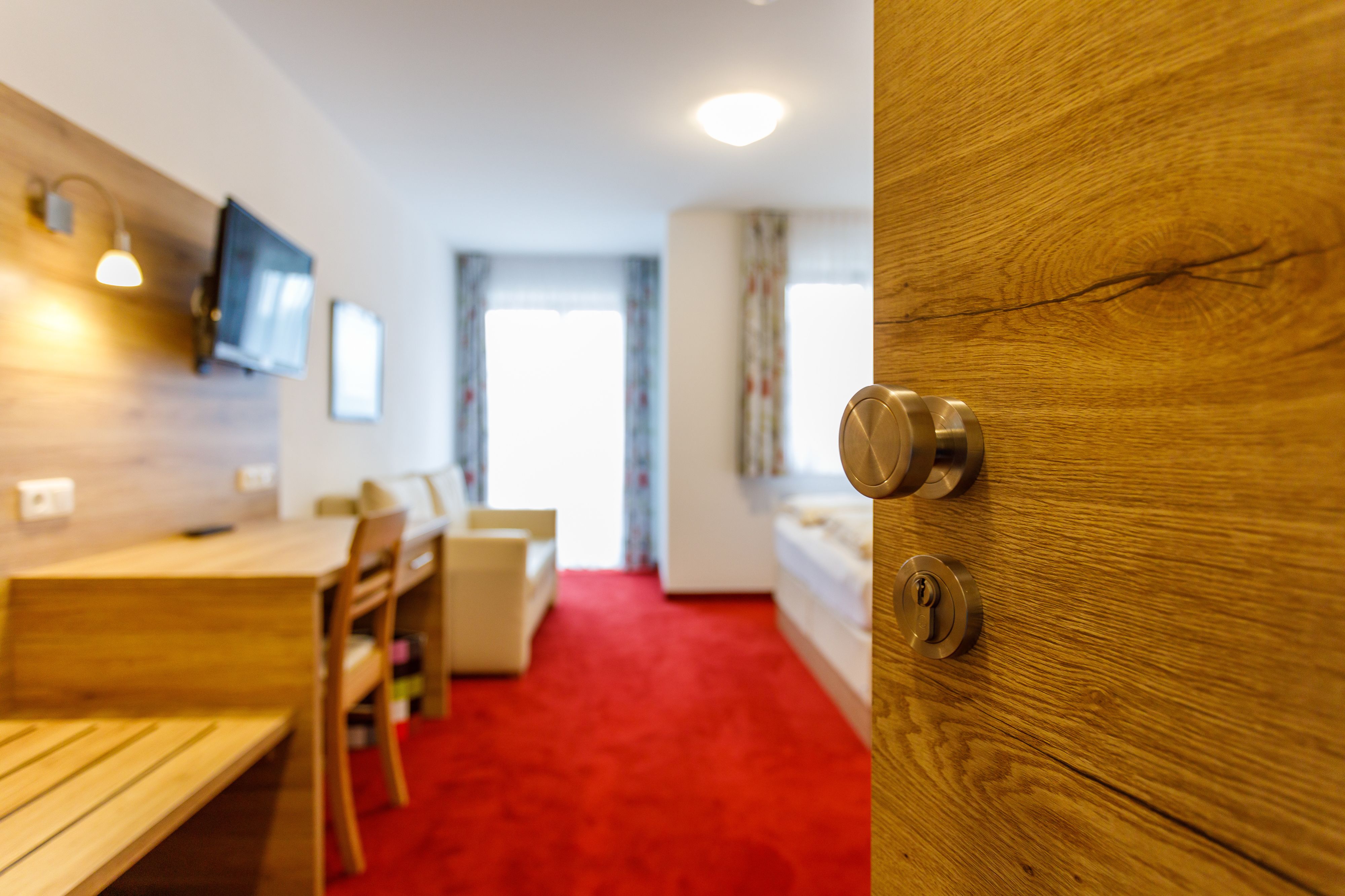 A modern room with a wooden door, a red carpet, a wooden table, and a television mounted on the wall.