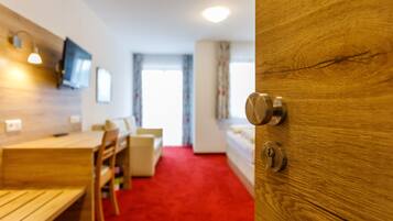 A modern room with a wooden door, a red carpet, a wooden table, and a television mounted on the wall.