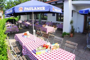 An outdoor dining area with tables covered in checkered tablecloths and blue umbrellas labeled "PAULANER." - Landhotel und Gasthaus Wiedmann (Eresing)