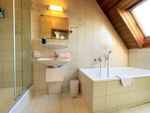 A bathroom with a bathtub, a sink, a mirror, and a shower. - Landhotel und Gasthaus Wiedmann (Eresing)