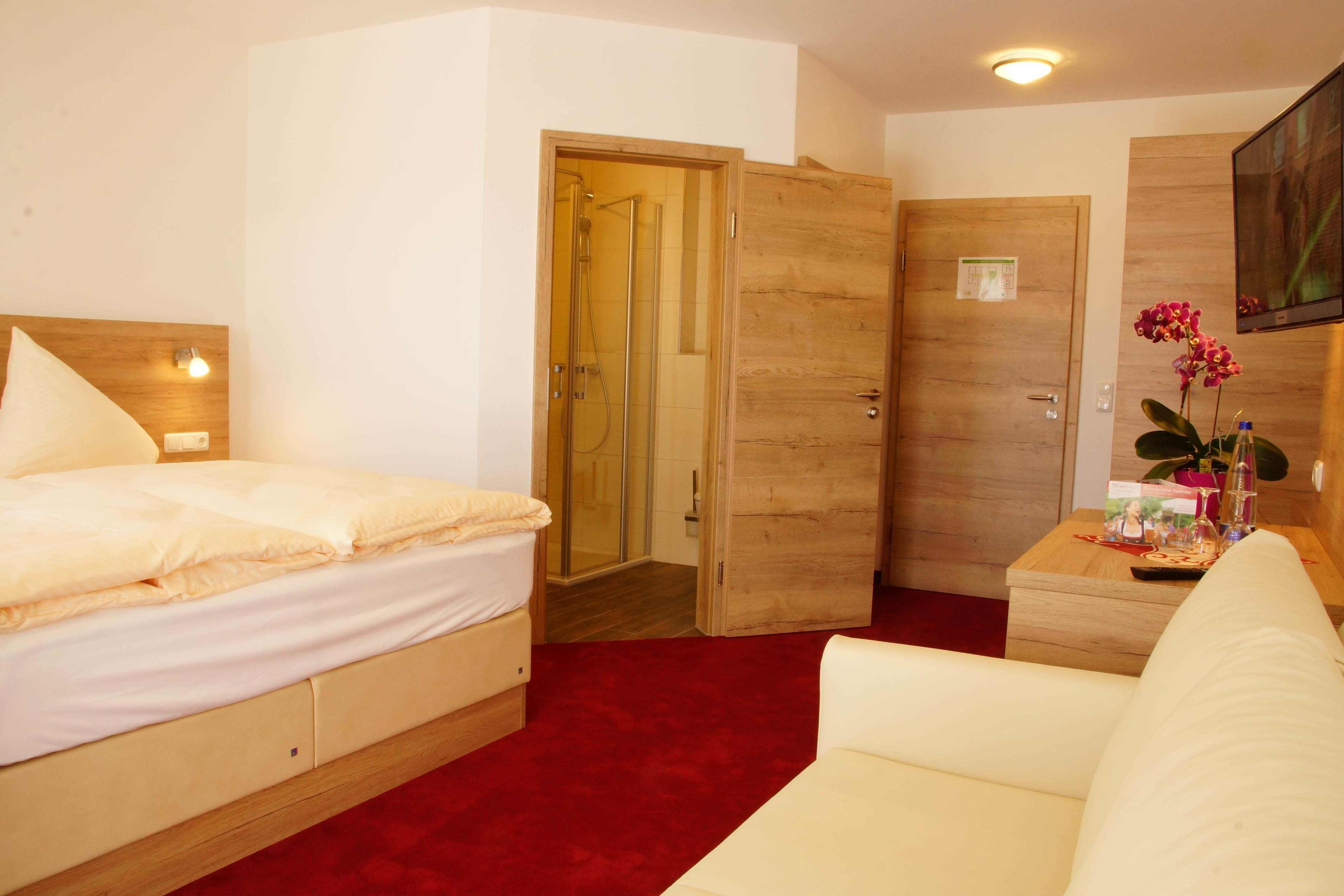 A hotel room with a bed, a wooden wardrobe, a wooden desk with a plant, and a television on the wall.