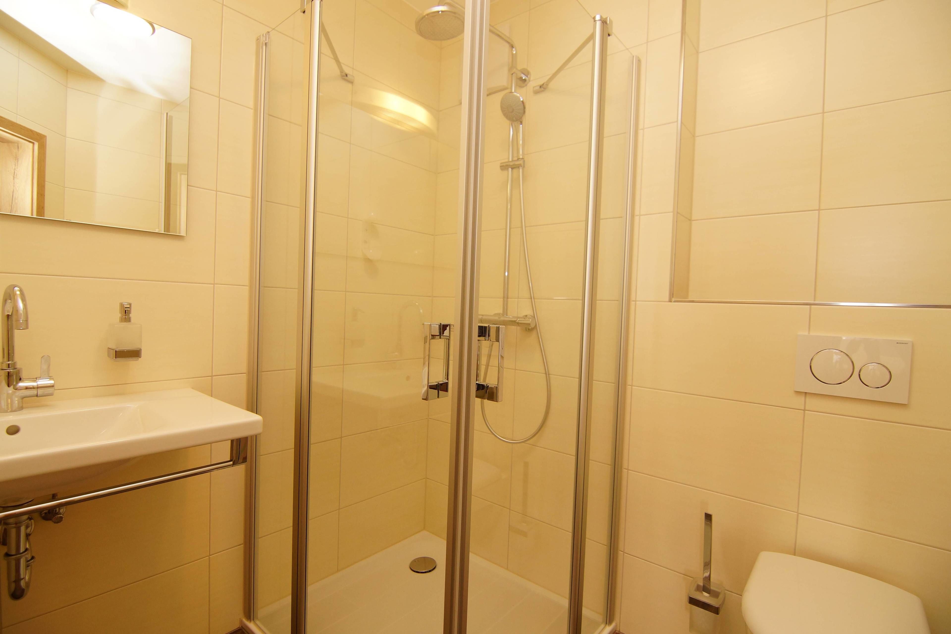 Ein modernes Badezimmer mit einer Duschkabine, einem Waschbecken mit Chromarmatur und einer Toilette.