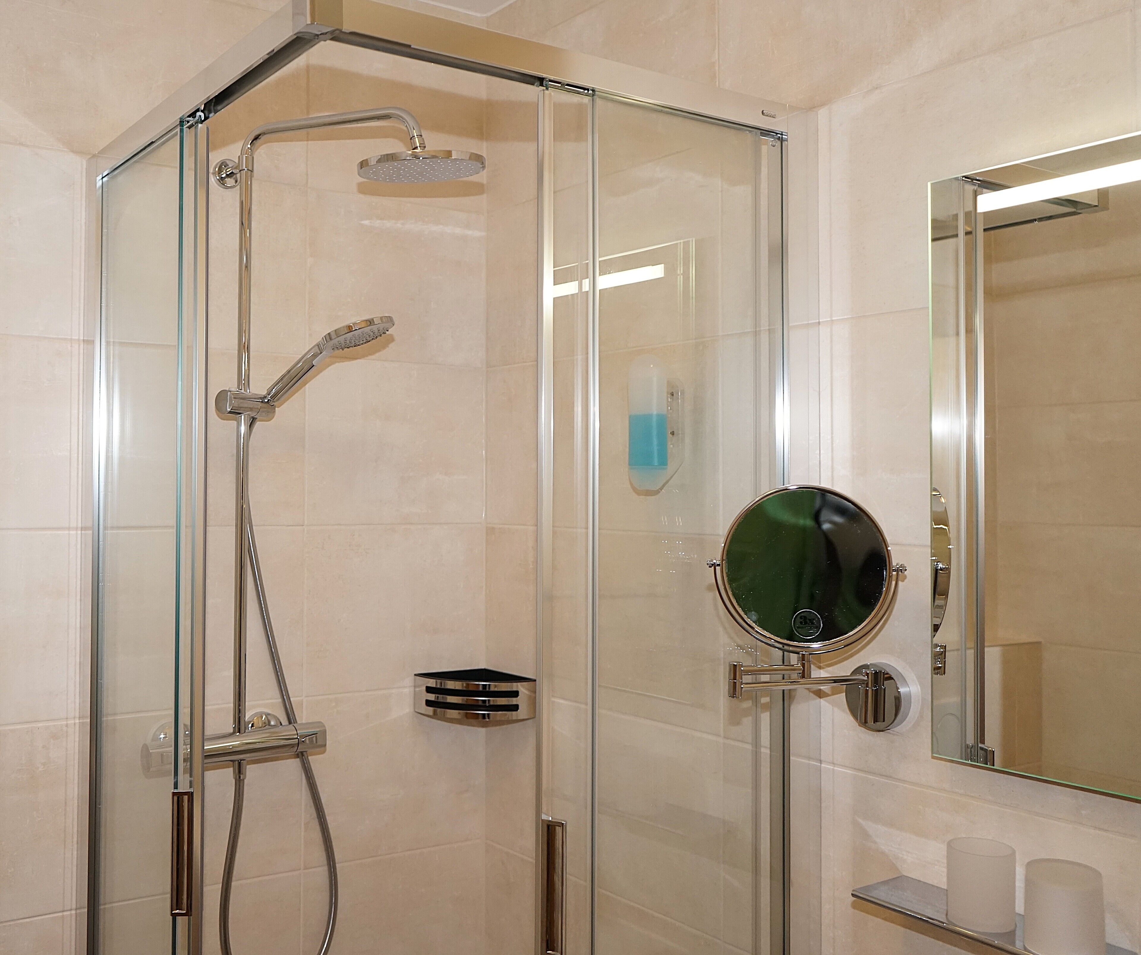 A glass-enclosed shower with a handheld showerhead and a wall-mounted faucet.
