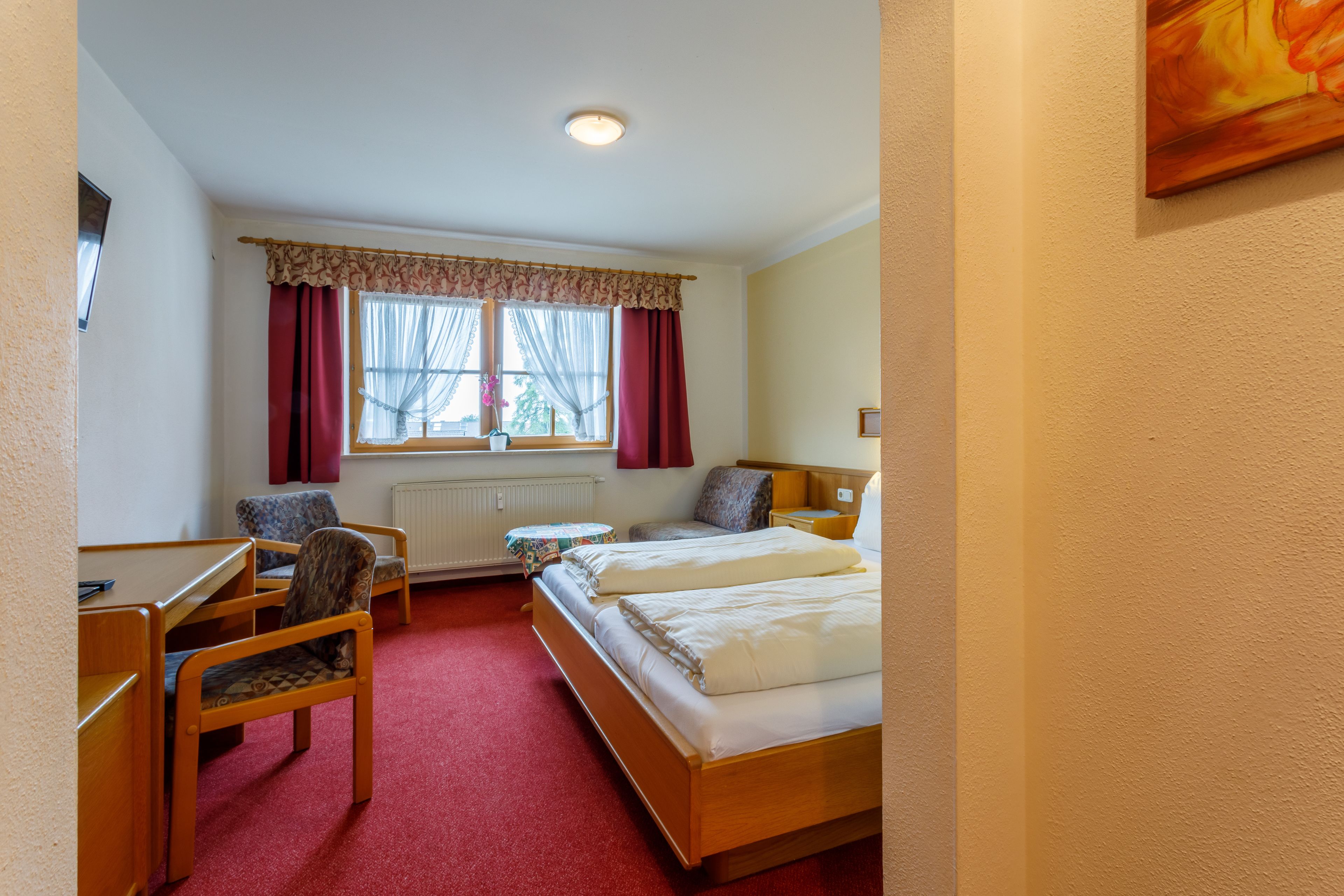 Ein Hotelzimmer mit Bett, zwei Stühlen, einem Schreibtisch und einem fensterbepflanzten Fenster.