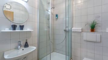 A modern bathroom with a glass-enclosed shower, a round mirror, a white sink, and a potted plant.