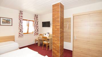 A bedroom with a bed, a desk, a chair, a TV, a wooden wardrobe, and a brick fireplace.