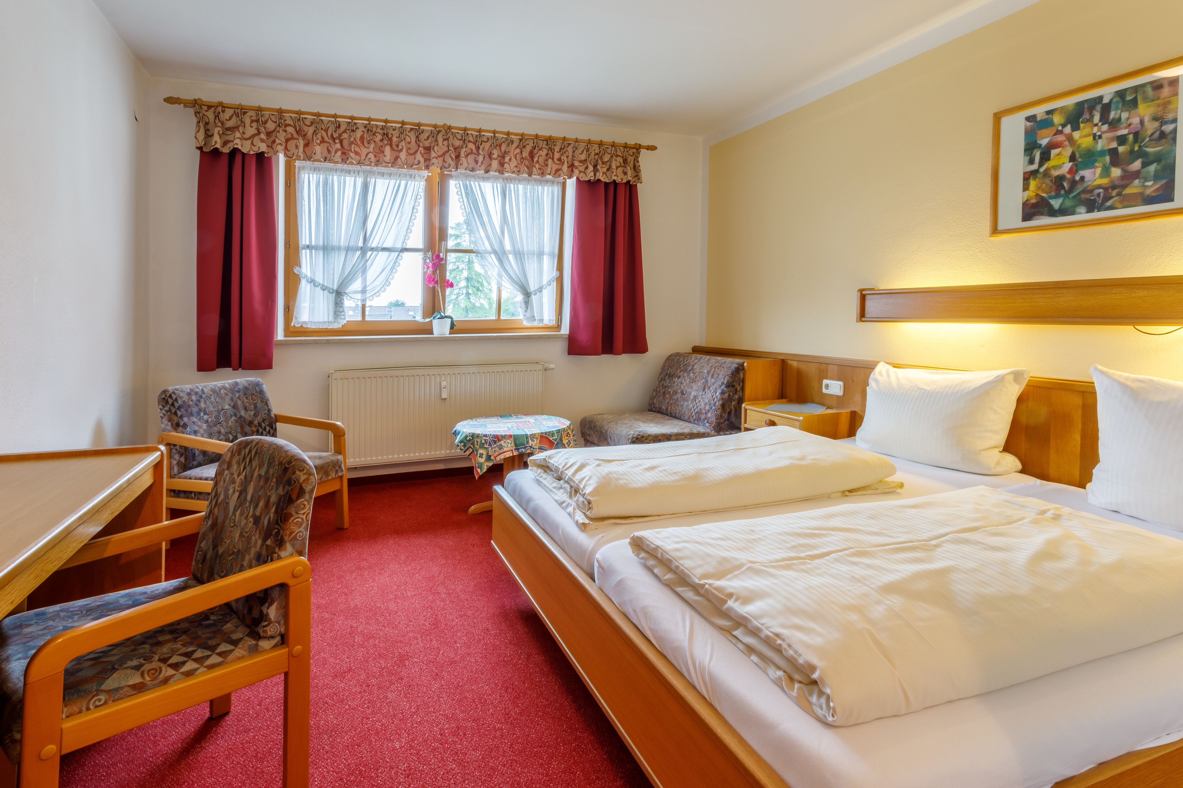 A hotel room with a bed, two chairs, a small table, and a window with curtains.