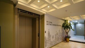 An elevator with a cityscape mural on the wall, a potted plant, and a ceiling with recessed lighting. - Star Guest House (Seoul)
