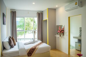 A hotel room with a bed, a small desk, a mirror, and a window with curtains. - The Sunflower Holiday Hostel (Choeng Thale)