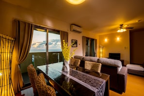 A living room with a dining table, sofa, and a view of the ocean. - United Resort Yomitan (Yomitan)