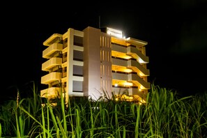 A multi-story hotel with balconies, a sign indicating it is a United Resort, and surrounded by tall grass. - United Resort Yomitan (Yomitan)