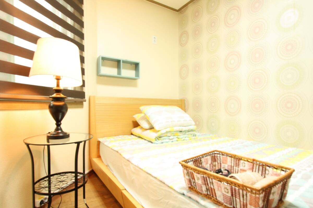 Une chambre à coucher avec un lit, une table de chevet avec une lampe, une étagère fixée au mur et un papier peint à motifs.