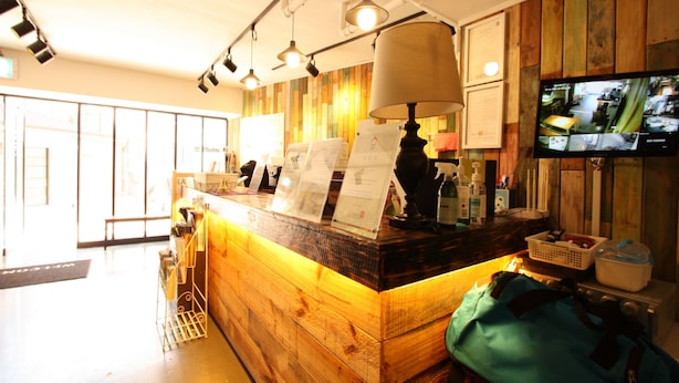 A reception area with a wooden counter, a large lamp, a television displaying multiple cameras, and a sign with text. - Welcome Guesthouse Myeongdong (Seoul)