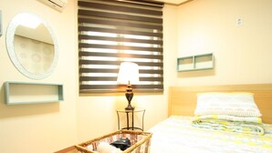 A neatly arranged bedroom with a bed, a bedside lamp, a wicker basket, a mirror, and a window with blinds. - Welcome Guesthouse Myeongdong (Seoul)