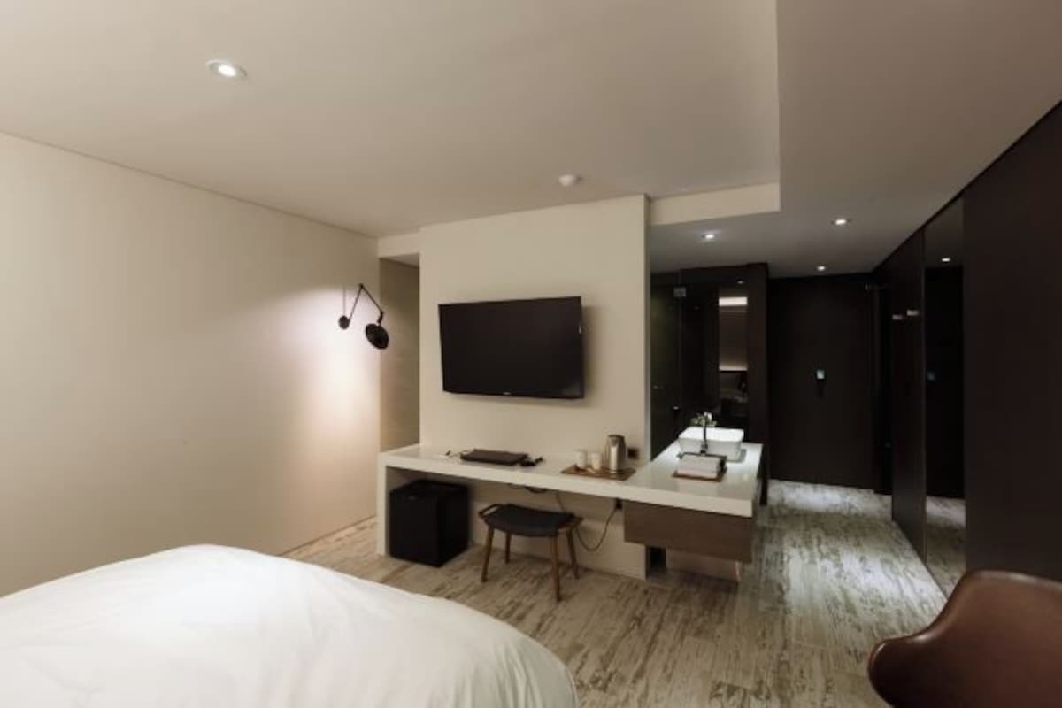 A modern hotel room with a bed, a desk, a TV, and a small seating area.
